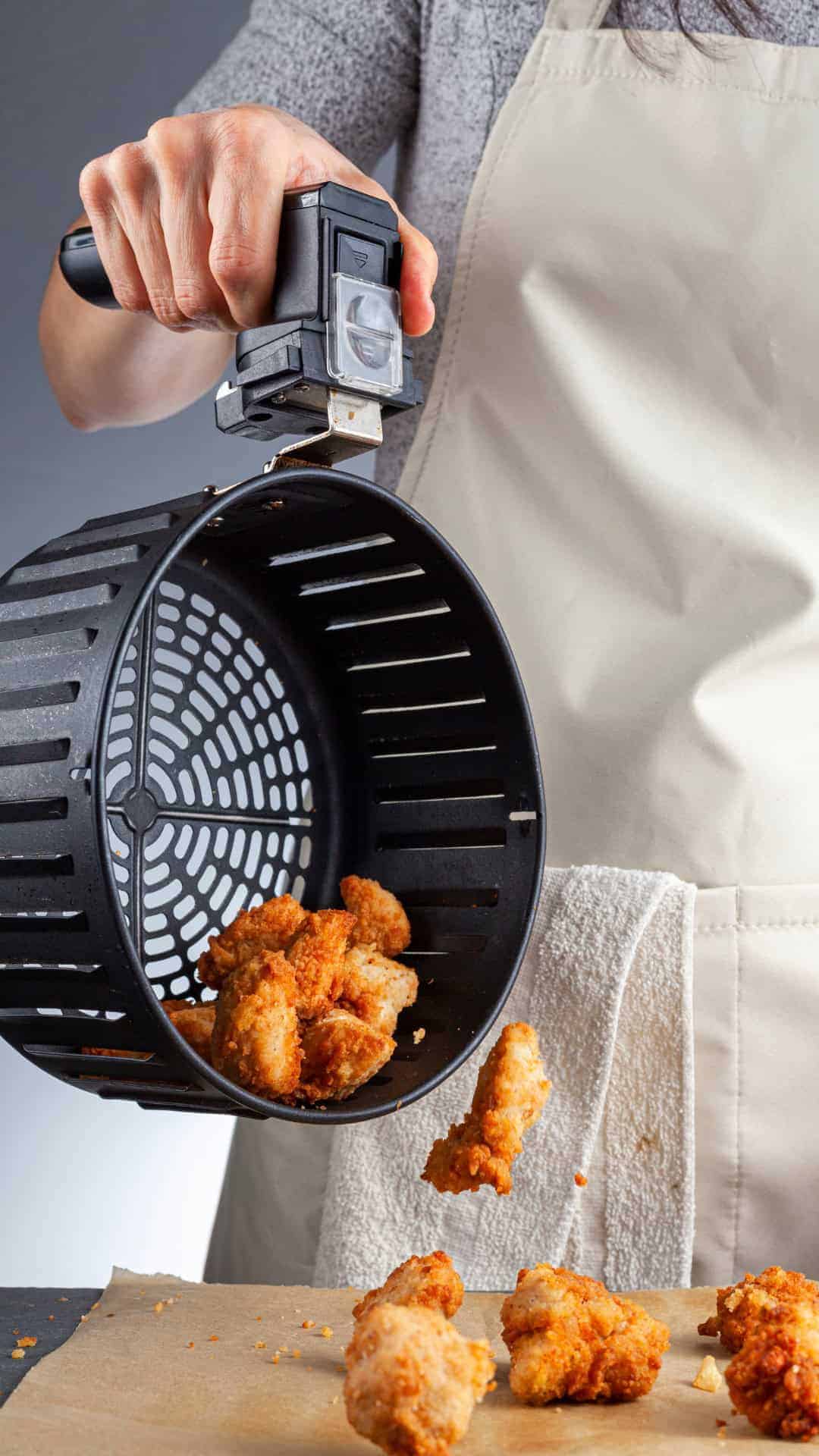 Frittierte Teile werden aus dem Korb einer Heißluftfritteuse auf ein Backblech gekippt