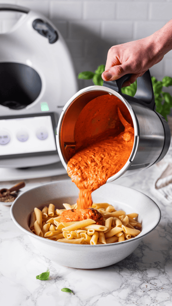 Tomatensosse wird aus dem Thermomix Mixtopf auf eine Schüssel Nudeln gegossen.